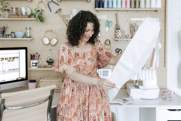 Megan Nielsen opening one of her sewing patterns in front of her plywood pegboard wall sewing workspace 